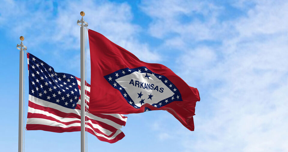 Arkansas state flag waving with the national flag of the United States of America on a clear day.