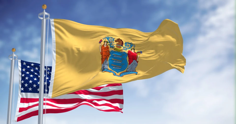 New Jersey state flag waving along with the national flag of the United States of America, with clear sky in the background.