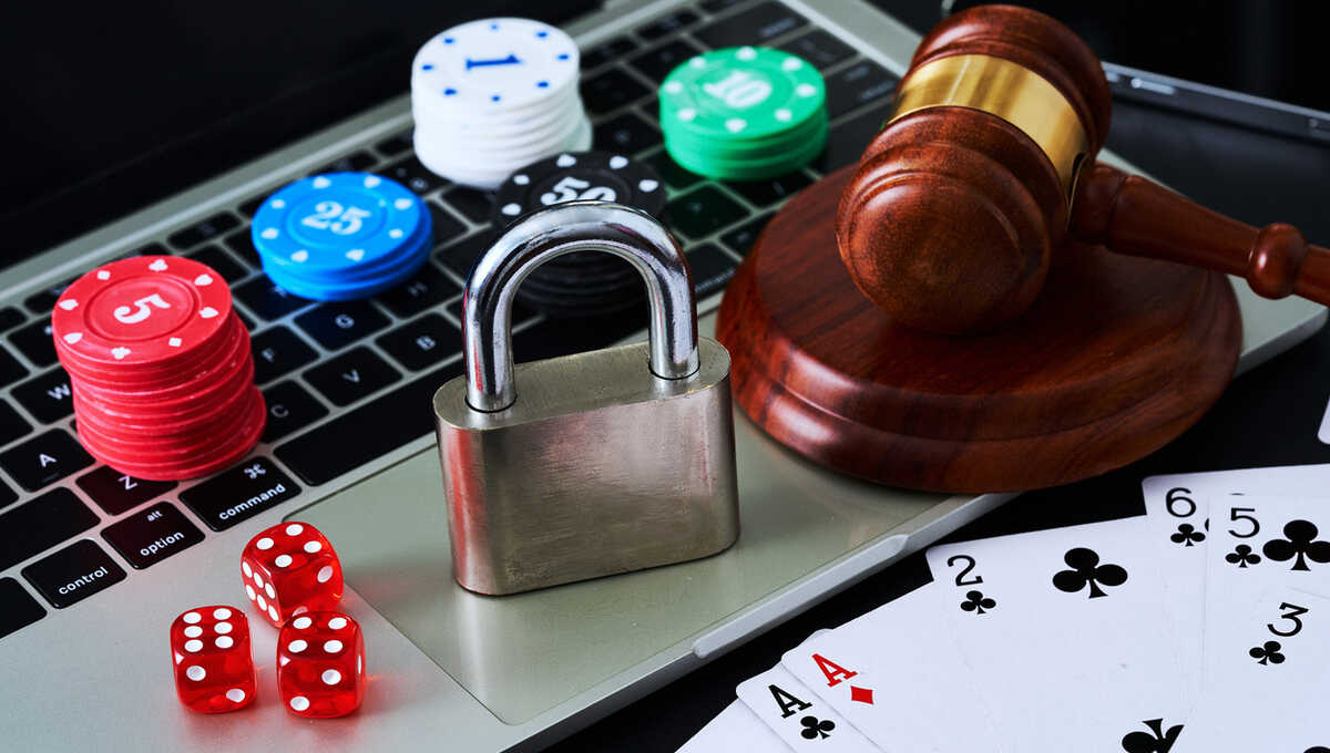 A laptop with poker chips, a padlock, dice, playing cards and a gavel over it