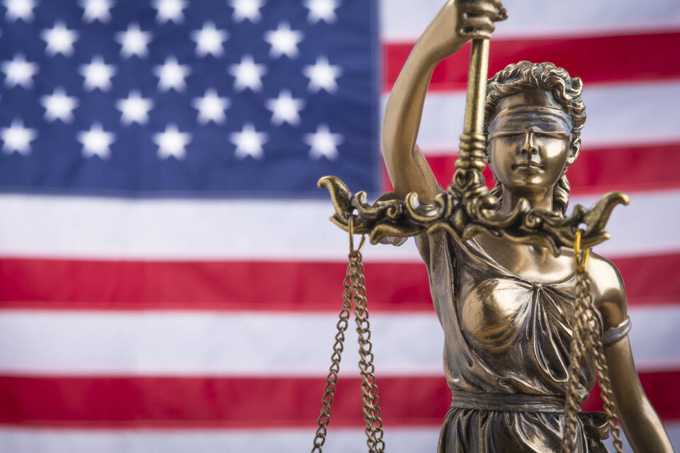 The statue of justice Themis or Justitia, the blindfolded goddess of justice against a flag of the United States of America